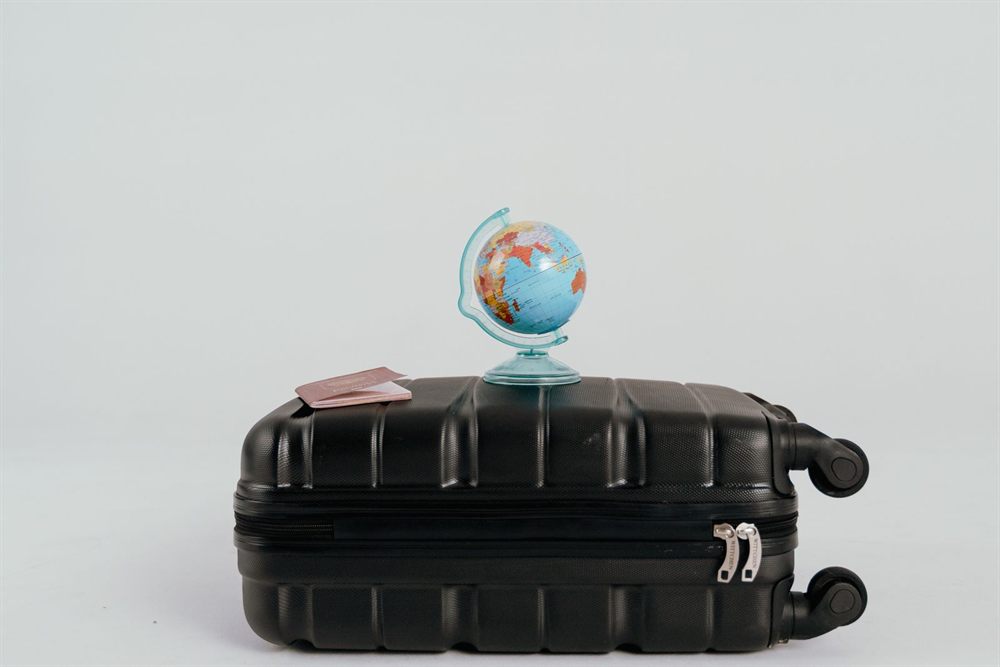 Small globe and passport resting on a black suitcase
