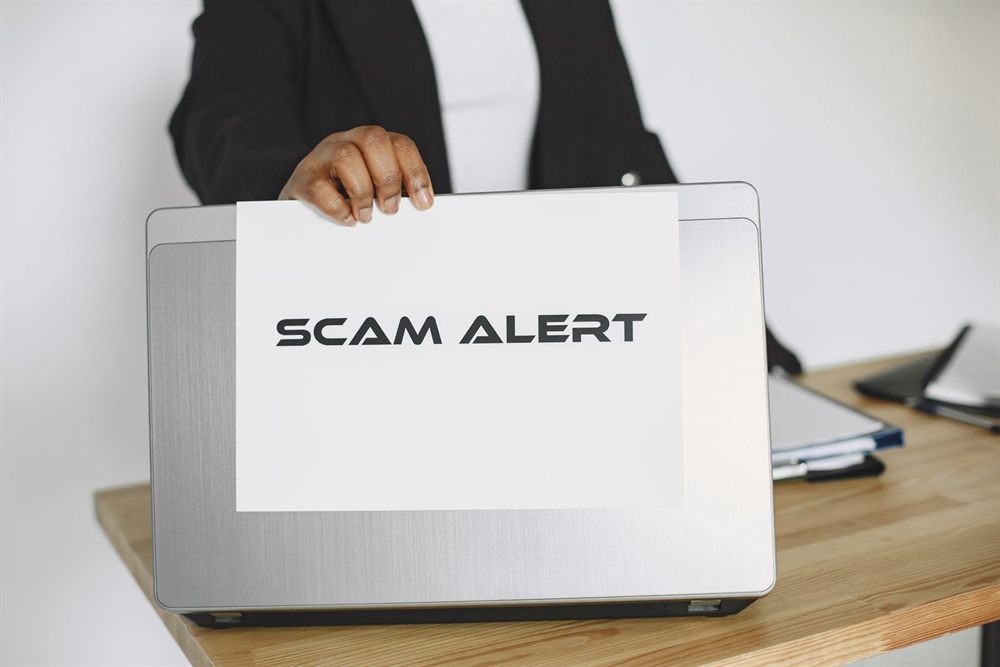 Person holding a scam alert sign in front of a laptop