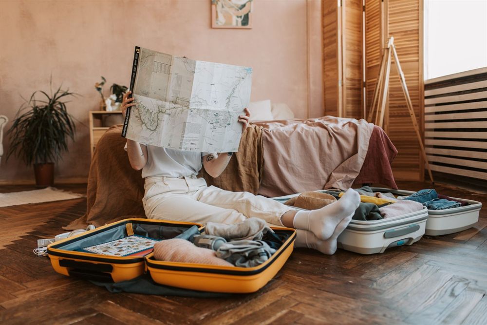 Traveler reading a paper map beside half-packed suitcases